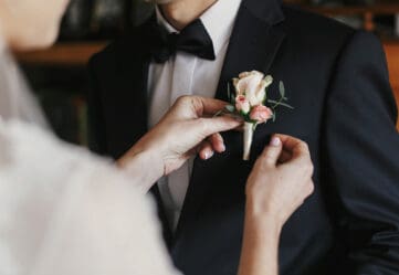 Groom's mother pinning on his boutonniere. Close up of hands and flower.