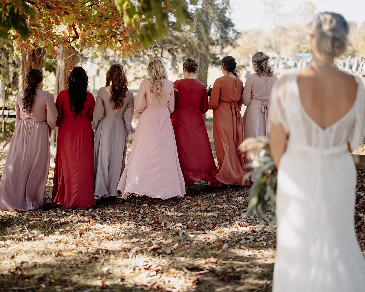 Bride getting ready to reveal her dress to bridesmaids under a beautiful fall oak tree.
