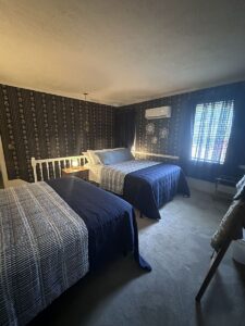 This is an image of The Bridesmaids' Retreat. An open loft area with two queen-sized beds and a half bath. Beds are comfortably appointed with blue and white bedding and multiple pillows. The floor is carpeted with new light grey plush carpet.