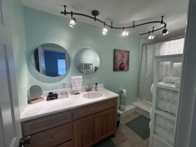 This is a photo of the downstairs master bath at Ross Mansion at The Barns at Marengo Cave. It has a modern curvy overhead light with directional lighting, Twho mirrors and a raised shower.