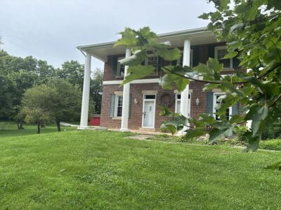 This image shows the outside of the Ross Mansion at The Barns at Marengo Cave. It is taken at daytime and has a green tree branch in the foreground.